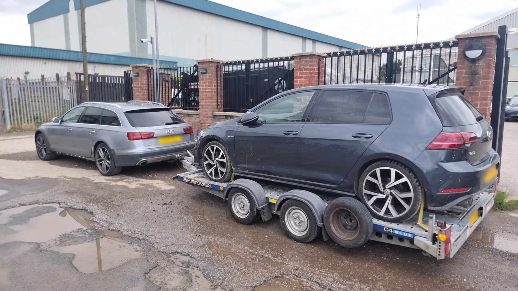 Car transporter carrying a hatchback, connected to a towing car; all registration plates obscured